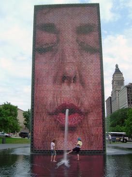 Two people frolicking in Crown Fountain in Millennium Park in Chicago as it spouts: Source Wikipedia